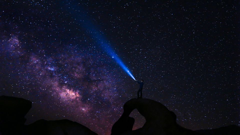 Imagen de un hombre sosteniendo una linterna contra al cielo estrellado.